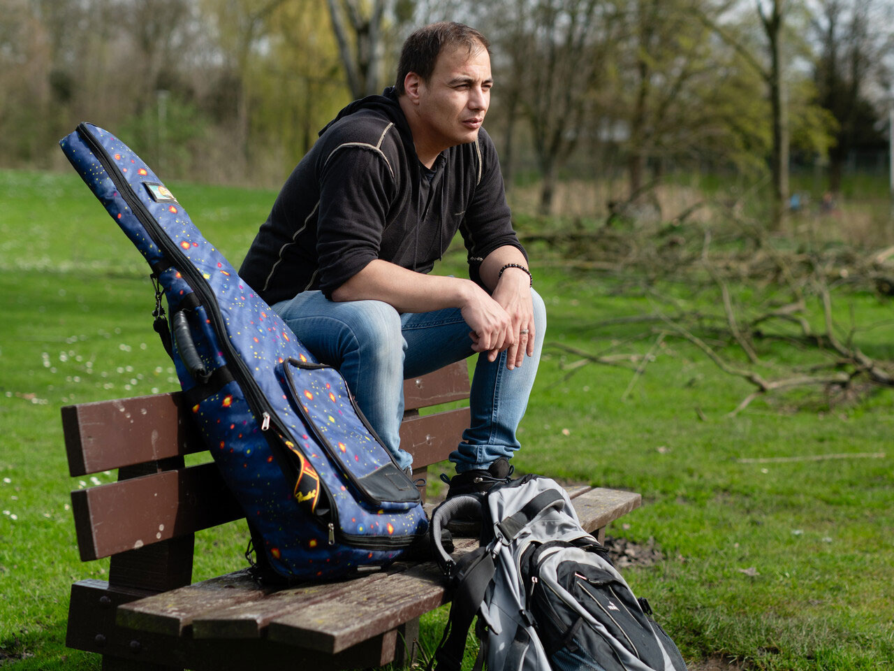 Man zit op bankje in park met gitaar en rugzak